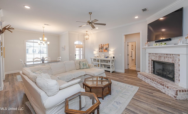 living room featuring a fireplace, ceiling fan with notable chandelier, wood-type flooring, and ornamental molding