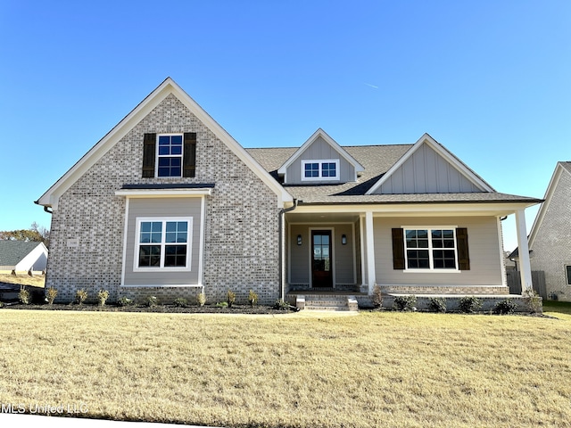 craftsman-style home featuring covered porch, a front yard, brick siding, and board and batten siding