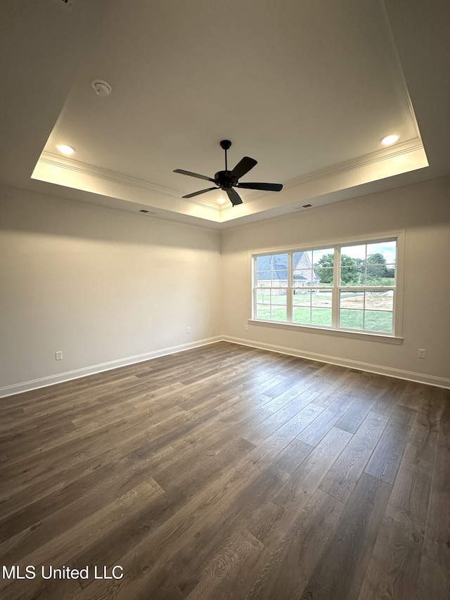 empty room with a tray ceiling, crown molding, baseboards, dark wood finished floors, and a ceiling fan