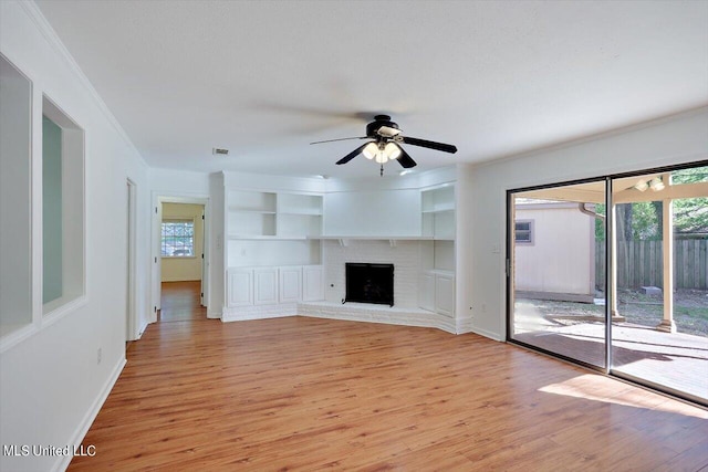 unfurnished living room with ceiling fan, ornamental molding, a fireplace, built in shelves, and light hardwood / wood-style floors