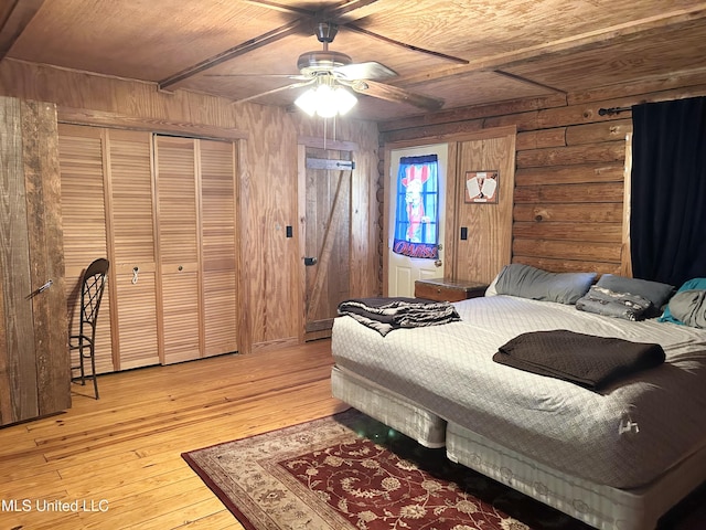 bedroom featuring wood ceiling, a closet, wood walls, ceiling fan, and light hardwood / wood-style flooring