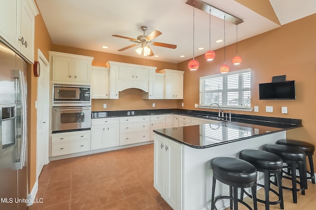 kitchen with appliances with stainless steel finishes, sink, a kitchen bar, pendant lighting, and white cabinets