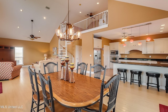 dining area featuring light hardwood / wood-style floors, ceiling fan with notable chandelier, and high vaulted ceiling