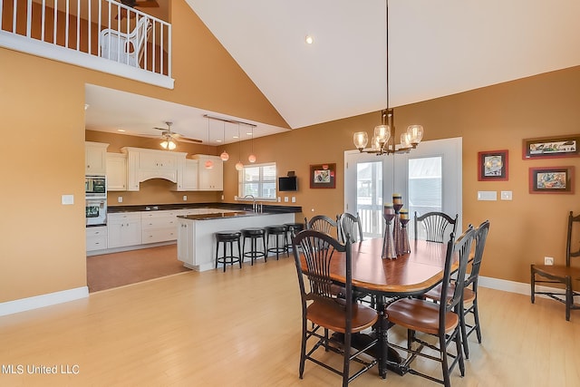 dining space with sink, light hardwood / wood-style flooring, ceiling fan with notable chandelier, and high vaulted ceiling