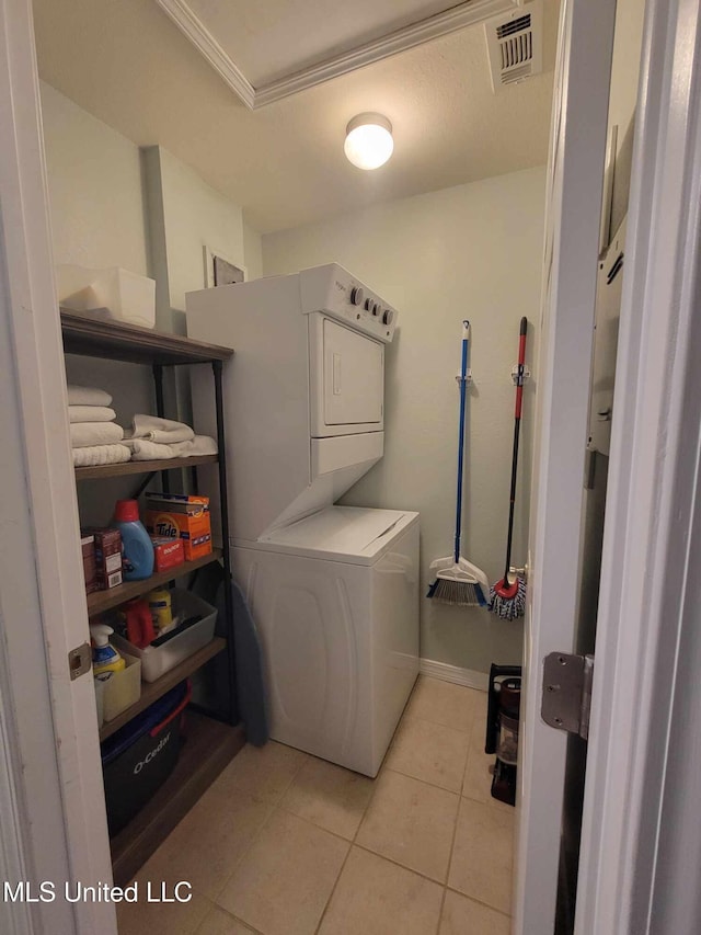 washroom with light tile patterned floors, stacked washer / drying machine, laundry area, visible vents, and ornamental molding