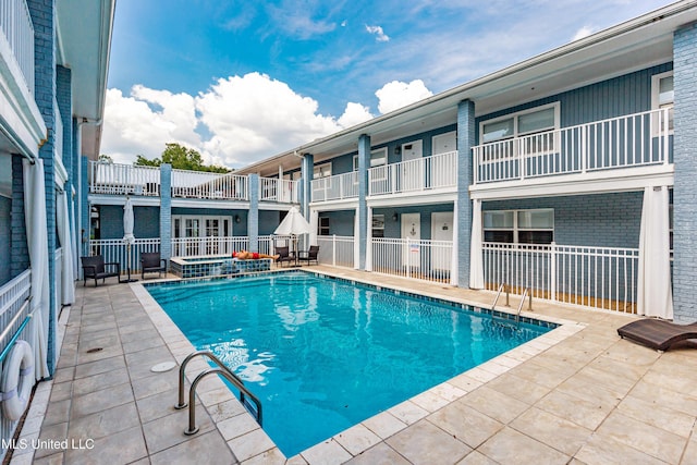 view of swimming pool featuring a pool with connected hot tub, fence, and a patio