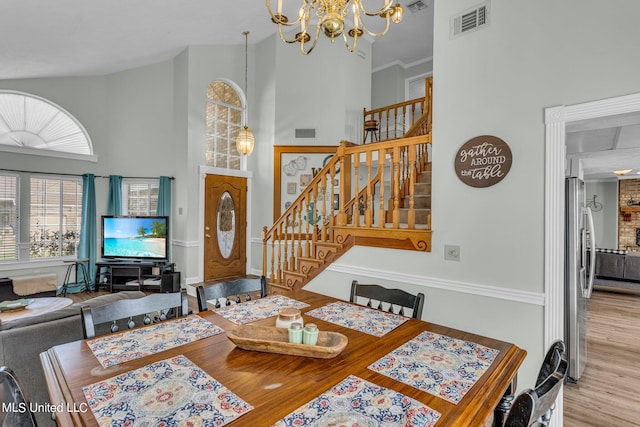 dining space with a towering ceiling, light hardwood / wood-style flooring, and a notable chandelier