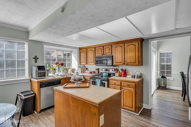 kitchen featuring tile countertops, a center island, appliances with stainless steel finishes, and light hardwood / wood-style flooring