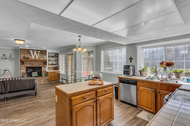 kitchen featuring dishwasher, a brick fireplace, light hardwood / wood-style floors, pendant lighting, and tile counters