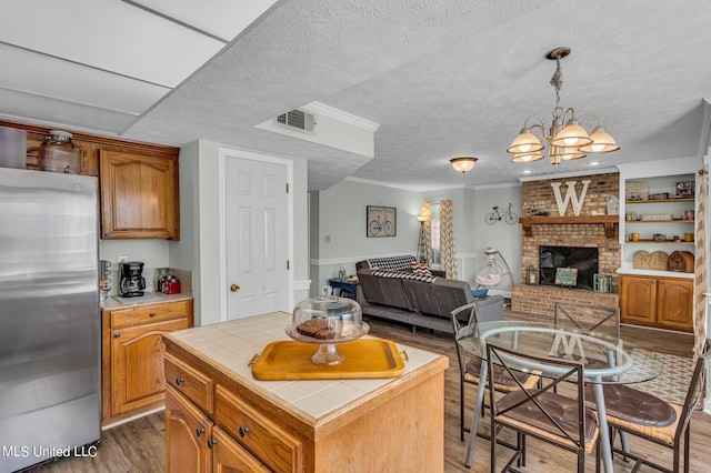 kitchen with a center island, a brick fireplace, dark hardwood / wood-style flooring, tile counters, and stainless steel refrigerator