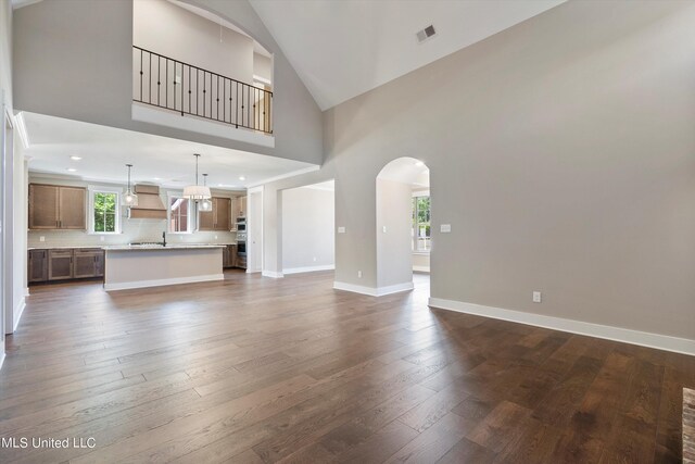 8025 Old Addison Dr, Olive Branch, MS 38654 - unfurnished living room featuring arched walkways, high vaulted ceiling, dark wood-type flooring, and baseboards