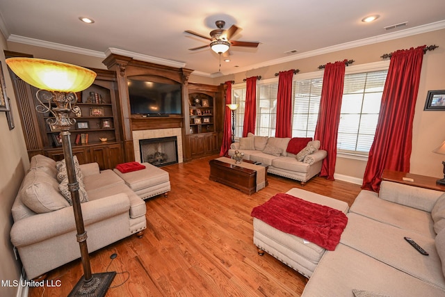 living room featuring a tiled fireplace, hardwood / wood-style floors, crown molding, and ceiling fan