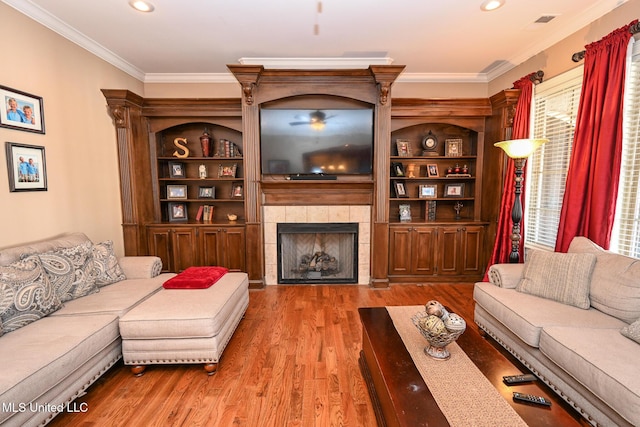 living room with hardwood / wood-style flooring, ornamental molding, a tiled fireplace, and a wealth of natural light