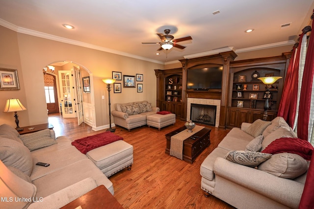 living room with hardwood / wood-style flooring, ceiling fan, crown molding, and a tiled fireplace