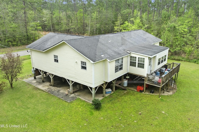 back of house with a view of trees, a yard, and a shingled roof
