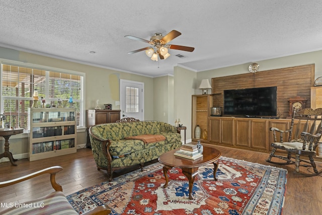 living area with hardwood / wood-style floors, ceiling fan, crown molding, and visible vents