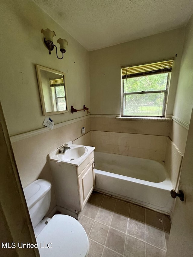 bathroom featuring a tub to relax in, toilet, a textured ceiling, vanity, and tile patterned flooring