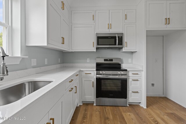 417 4th Ave, Pass Christian, MS 39571 - kitchen featuring stainless steel appliances, white cabinetry, light wood-type flooring, and light stone countertops