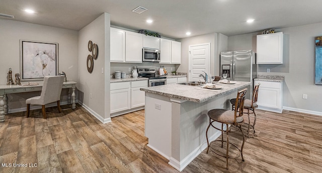 kitchen with an island with sink, stainless steel appliances, light wood-type flooring, white cabinets, and sink