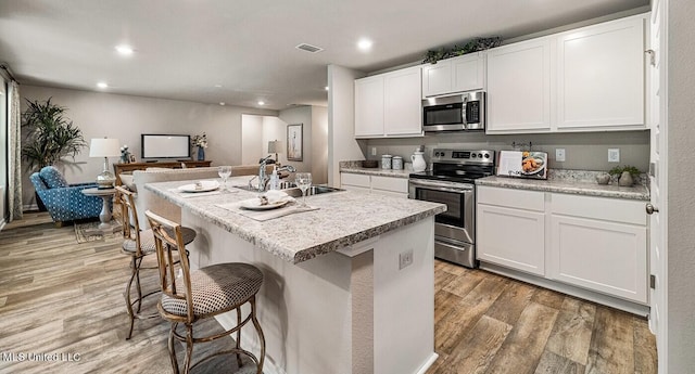 kitchen with white cabinetry, appliances with stainless steel finishes, a kitchen island with sink, light wood-type flooring, and a breakfast bar