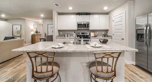 kitchen featuring sink, white cabinetry, stainless steel appliances, and an island with sink