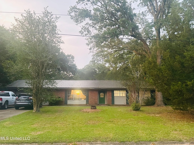 ranch-style house featuring concrete driveway, brick siding, metal roof, and a front lawn
