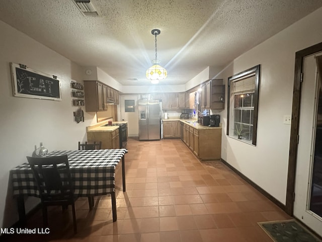 kitchen with black range with gas stovetop, stainless steel refrigerator with ice dispenser, light countertops, a sink, and hanging light fixtures