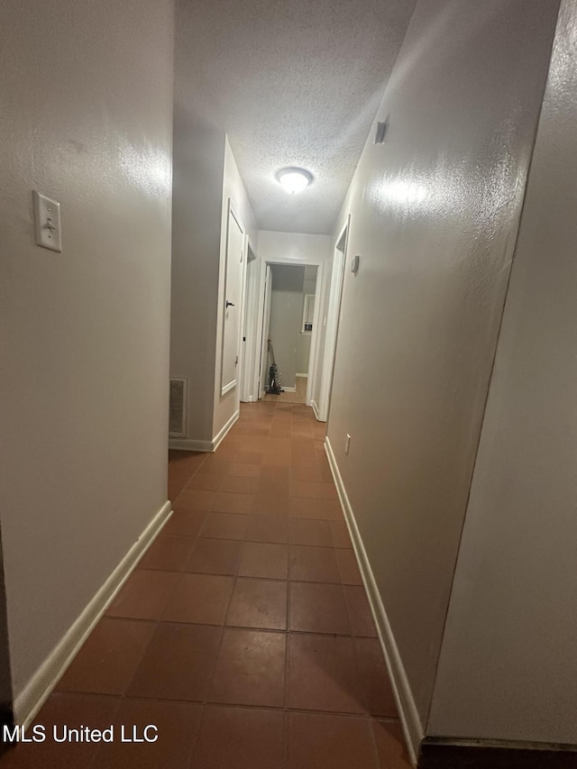 hall featuring baseboards, a textured ceiling, tile patterned floors, and visible vents