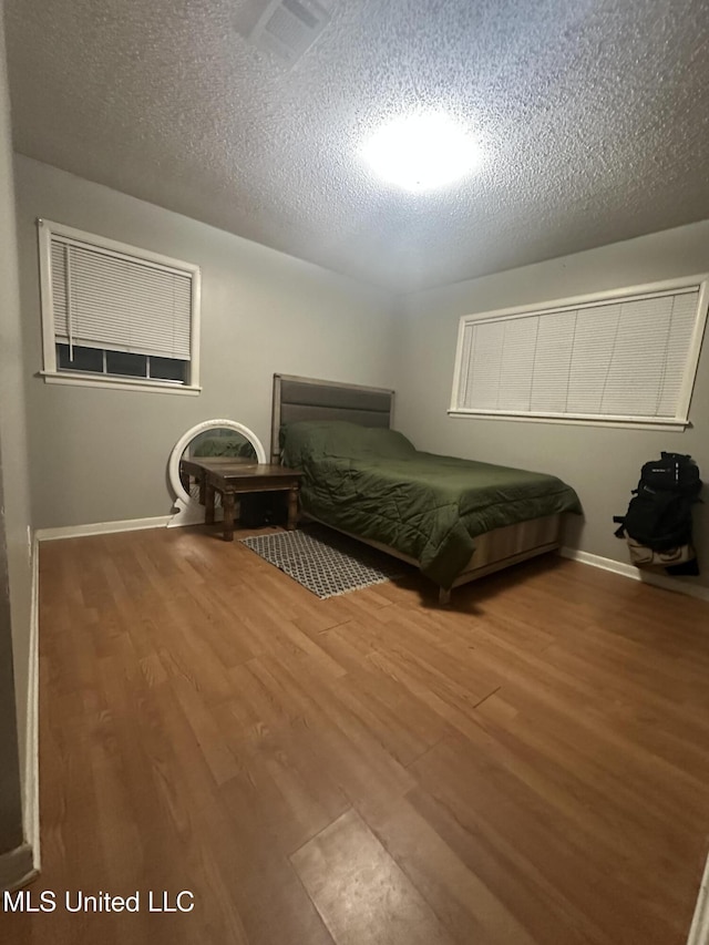 bedroom with baseboards, a textured ceiling, and wood finished floors