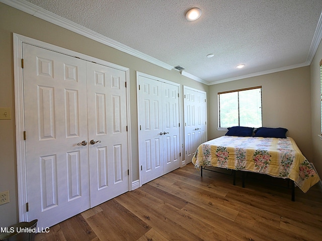 bedroom with wood finished floors, a textured ceiling, two closets, crown molding, and recessed lighting