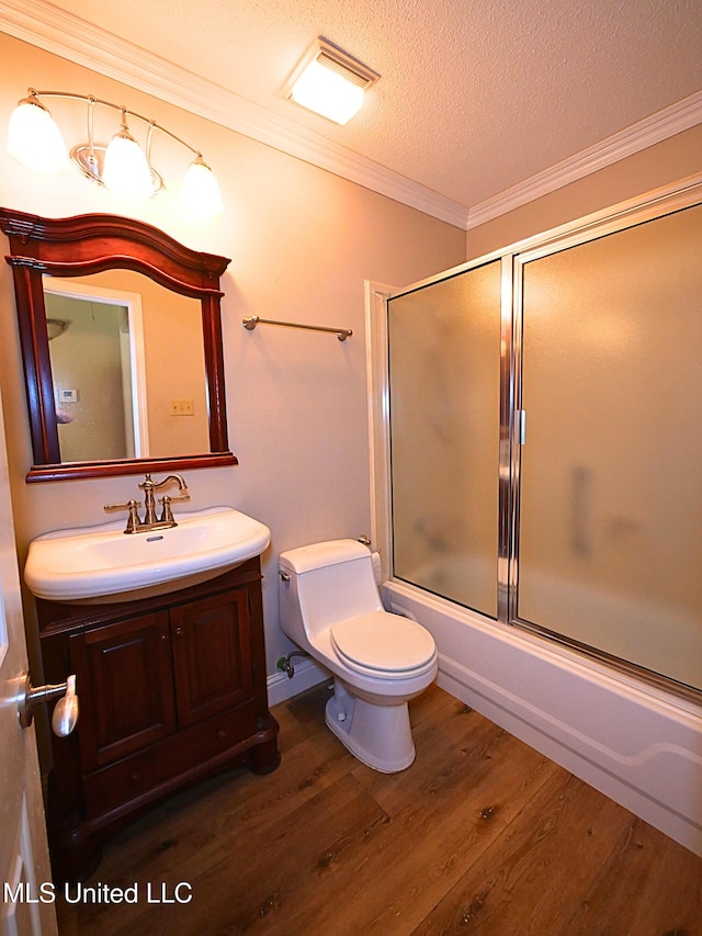 bathroom featuring wood finished floors, vanity, enclosed tub / shower combo, a textured ceiling, and ornamental molding