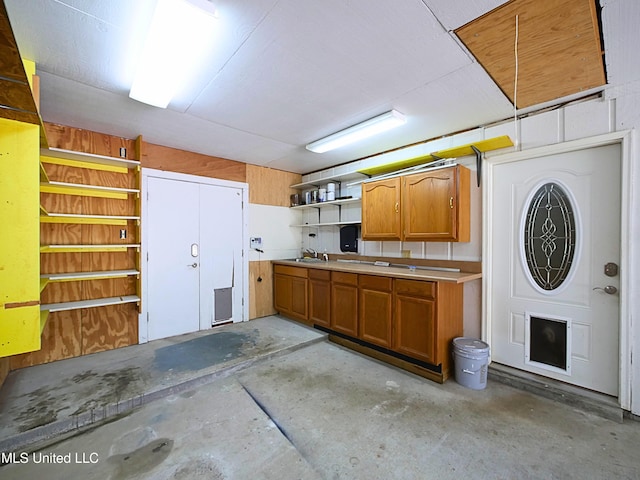 kitchen with concrete flooring, open shelves, brown cabinets, and a sink
