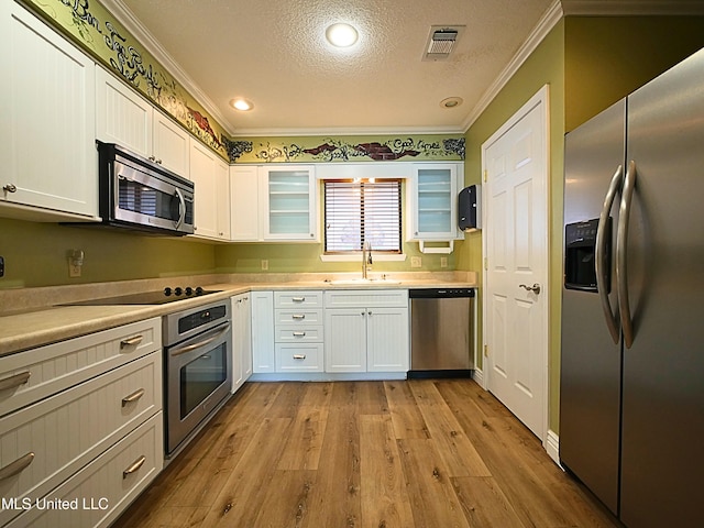 kitchen with appliances with stainless steel finishes, a sink, ornamental molding, white cabinets, and a textured ceiling