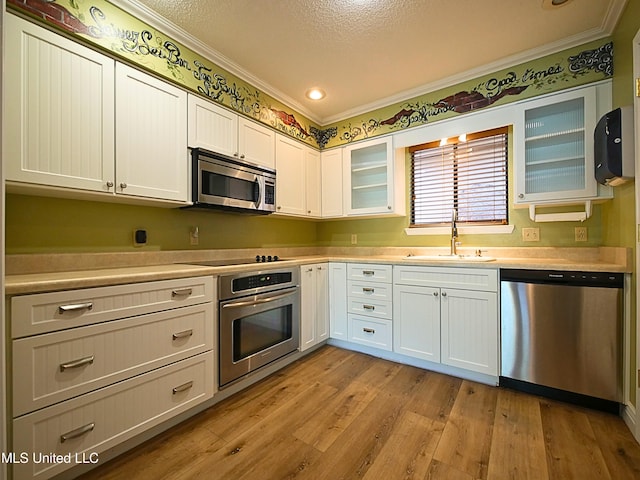 kitchen featuring stainless steel appliances, a sink, ornamental molding, light countertops, and white cabinets
