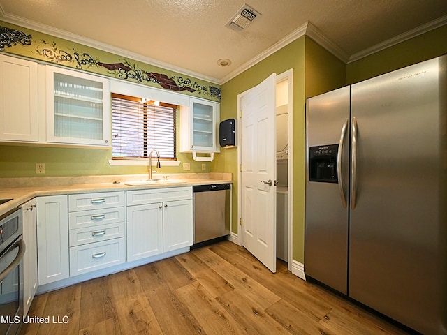 kitchen featuring appliances with stainless steel finishes, a sink, ornamental molding, light wood-style flooring, and white cabinetry