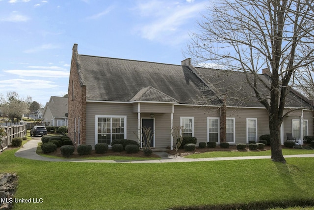 new england style home featuring a chimney, roof with shingles, a front yard, and fence