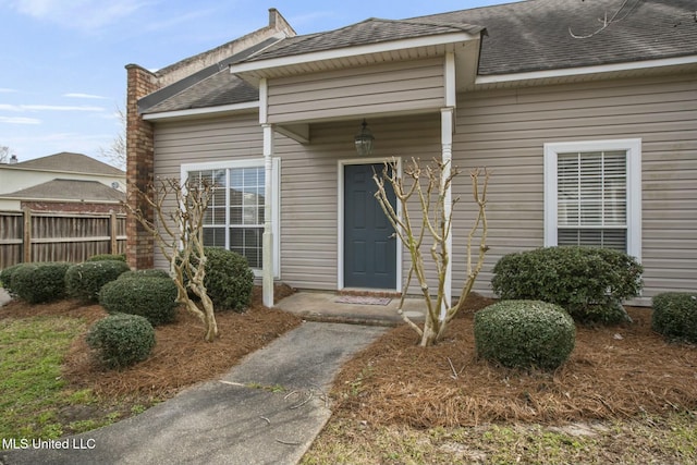 entrance to property featuring roof with shingles and fence