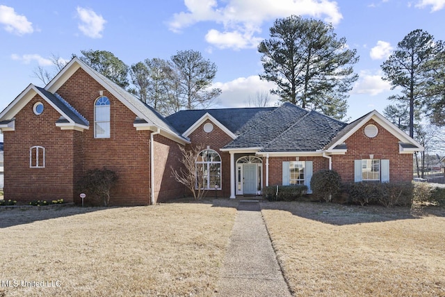 view of front facade with roof with shingles, brick siding, and a front lawn