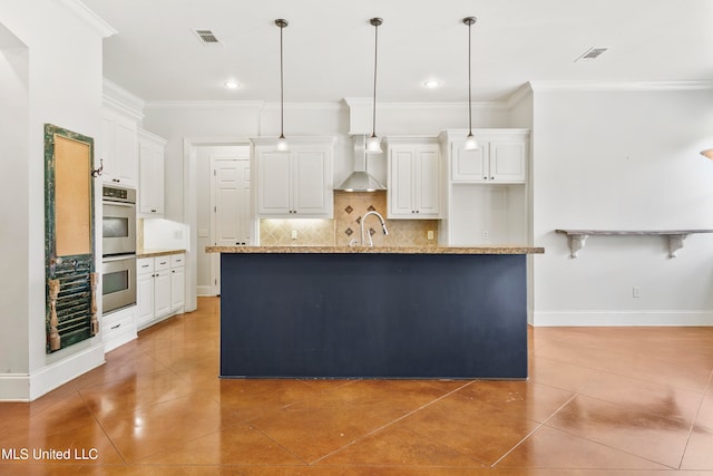 kitchen with wall chimney range hood, an island with sink, pendant lighting, white cabinets, and ornamental molding
