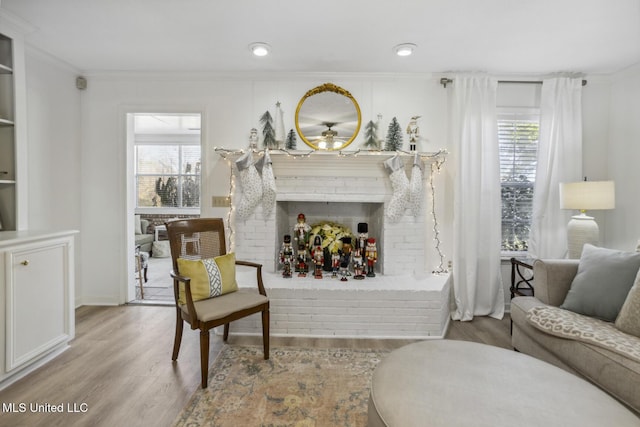 living area featuring ornamental molding, a brick fireplace, and light hardwood / wood-style flooring