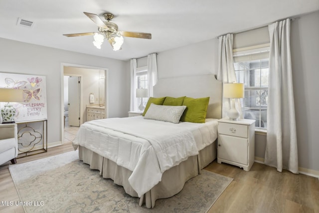 bedroom with ensuite bath, ceiling fan, light hardwood / wood-style flooring, and multiple windows