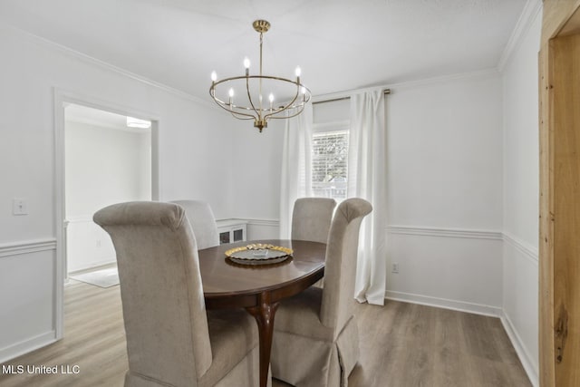 dining space with crown molding, light hardwood / wood-style flooring, and an inviting chandelier