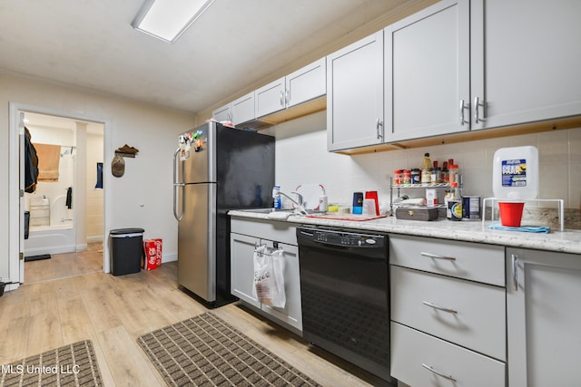 kitchen with white cabinetry, black dishwasher, light hardwood / wood-style floors, stainless steel fridge, and light stone counters