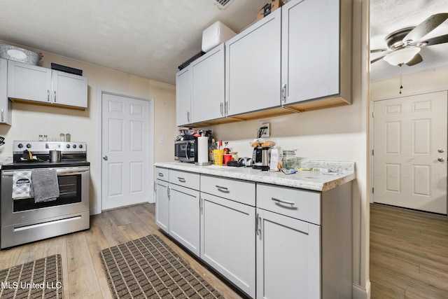 kitchen featuring white cabinets, ceiling fan, stainless steel electric range oven, and light hardwood / wood-style flooring