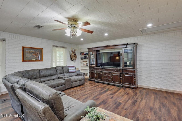 living room with brick wall, dark wood-type flooring, and ceiling fan