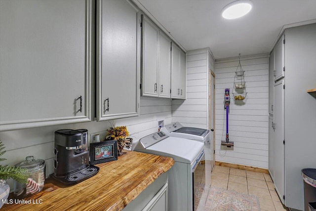 clothes washing area featuring cabinets, washer and dryer, wooden walls, and light tile patterned floors