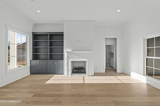 unfurnished living room with ornamental molding, light wood-type flooring, built in features, and a fireplace