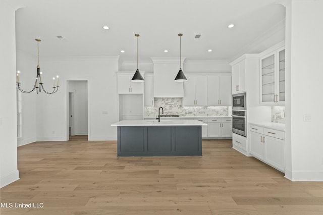 kitchen featuring white cabinetry, stainless steel appliances, hanging light fixtures, and a center island with sink