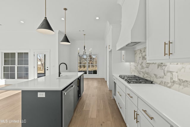 kitchen with decorative light fixtures, an island with sink, sink, white cabinets, and custom range hood