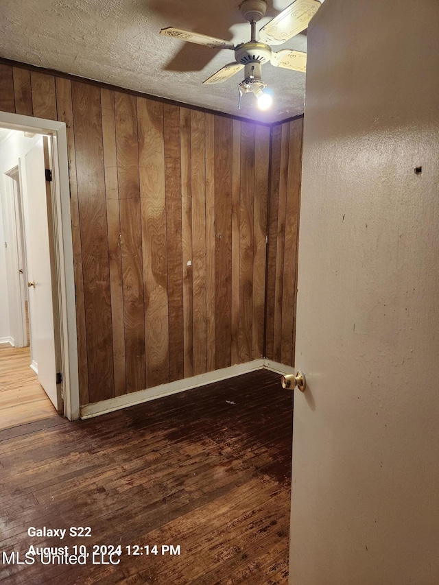 interior space with wooden walls, hardwood / wood-style flooring, a textured ceiling, and ceiling fan